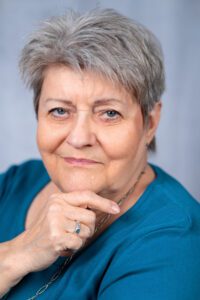 Portrait der Autorin Gabriele Walter in einem türkisenen Pullover vor einer grauen Wand